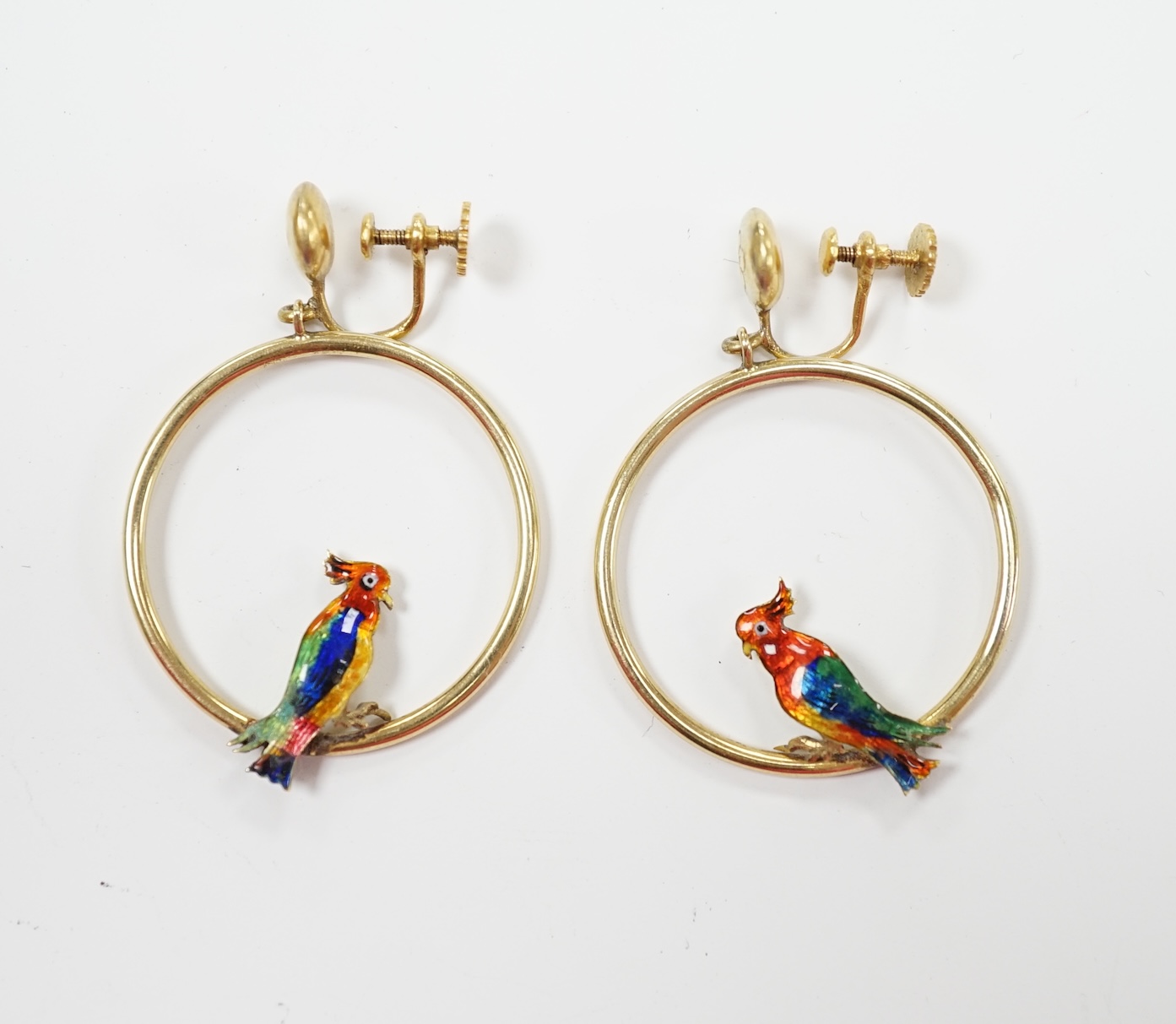A pair of early 20th century 15ct loop ear clips, with a polychrome enamelled parrot perched upon each, diameter 30mm, gross weight 7.3 grams.